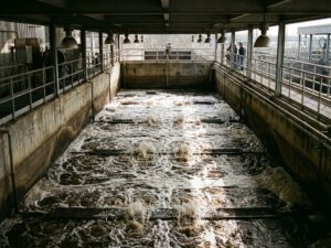 Abwasserkläranlage mit sprudelndem Belebungsbecken, Luftblasen steigen auf und erzeugen weißen Schaum auf braunem Wasser