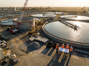 Abwasserbehandlungsanlage mit kreisförmigen Klärbecken, Baukränen und Arbeitern in Sicherheitswesten bei Erweiterungsarbeiten