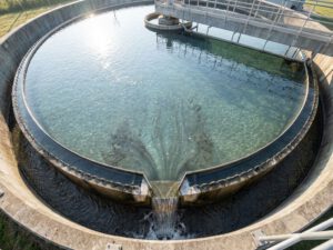 Kreisförmiges Nachklärbecken einer Kläranlage mit klarem Wasser und absetzenden Schlammpartikeln von oben fotografiert
