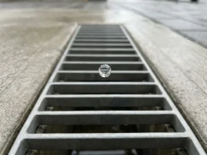 Regentropfen schwebt über Betonabflussrost mit geometrischen Mustern bei natürlichem Tageslicht