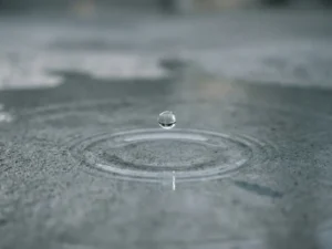 Wassertropfen schwebt über Betonoberfläche kurz vor dem Aufprall mit konzentrischen Wellen