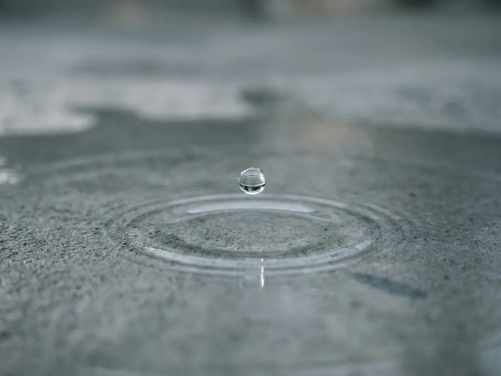 Wassertropfen schwebt über Betonoberfläche kurz vor dem Aufprall mit konzentrischen Wellen